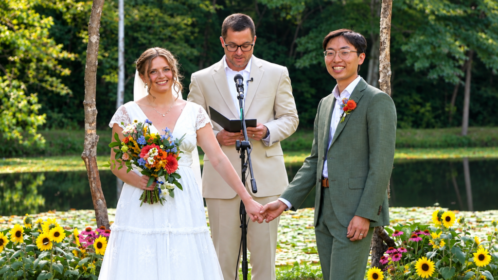 Emma and Michael holding hands during their outdoor wedding ceremony beside a pond