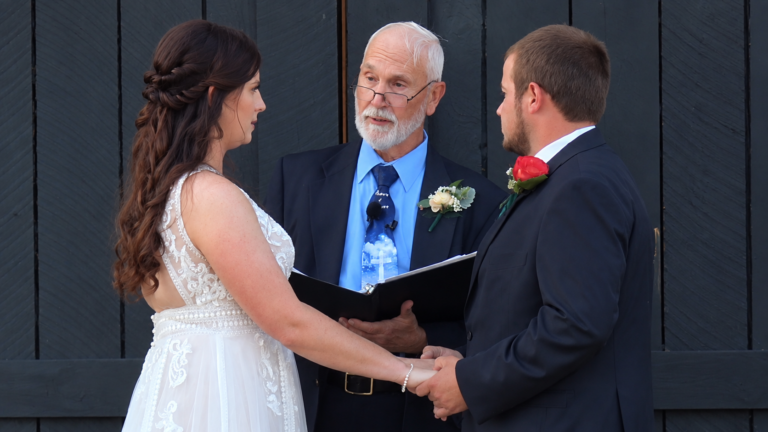 Kelsey and Cam holding hands during their wedding ceremony as the officiant speaks