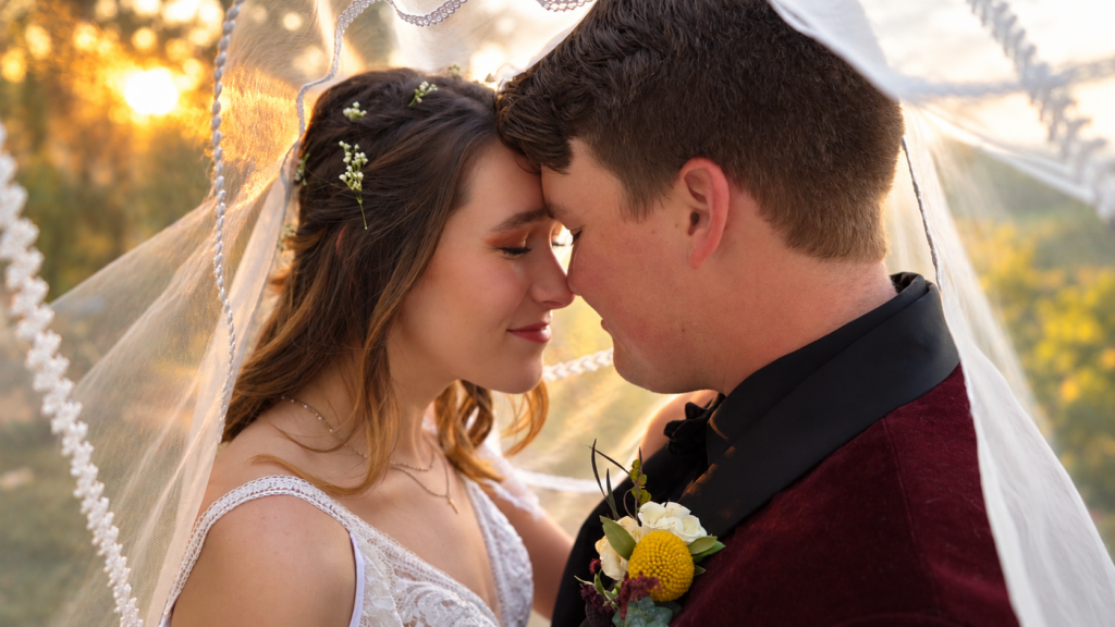 Bride and groom sharing a romantic moment beneath the veil at sunset
