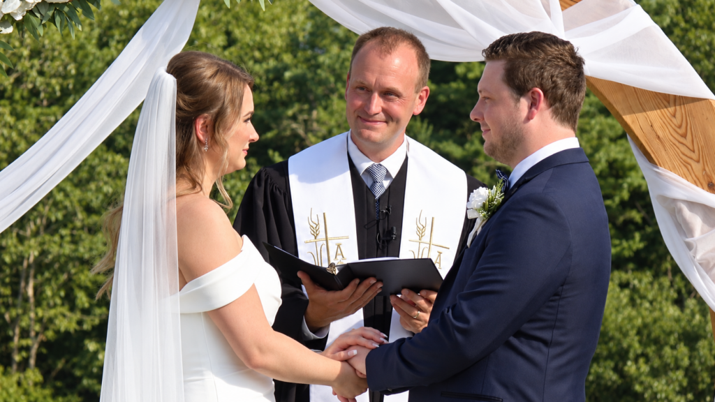 Bride and groom holding hands during their outdoor wedding ceremony as the officiant speaks